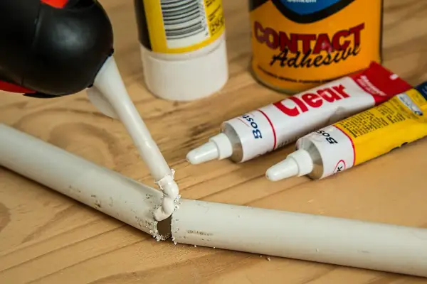 Aplikator z klejem naprawia pękniętą białą rurkę. Obok leżą tubki kleju, idealne, by dowiedzieć się, czym skleić plastik.