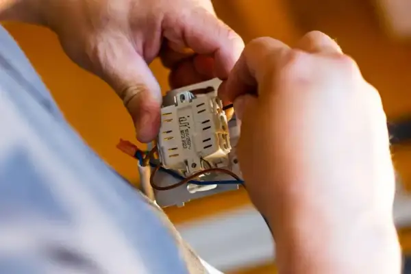 Ręce elektryka podłączają przewody do mechanizmu włącznika. Dowiedz się, ile kosztuje przyłącze prądu.