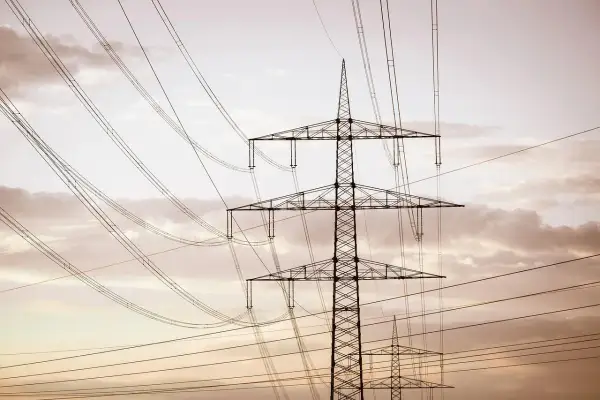 Wysoki słup na działce, który stoi tam od ponad 30 lat, otoczony siecią przewodów elektrycznych na tle zachmurzonego nieba.