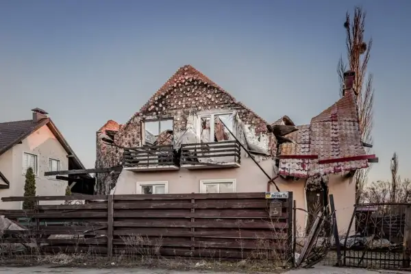 Zniszczony dom po ostrzale. Rozbiórka dachu i ścian, wybite okna, zniszczony płot.