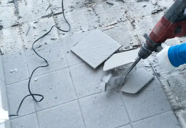Skuwanie płytek cena: młot udarowy kruszy szare płytki na podłodze, tworząc pył i gruz.