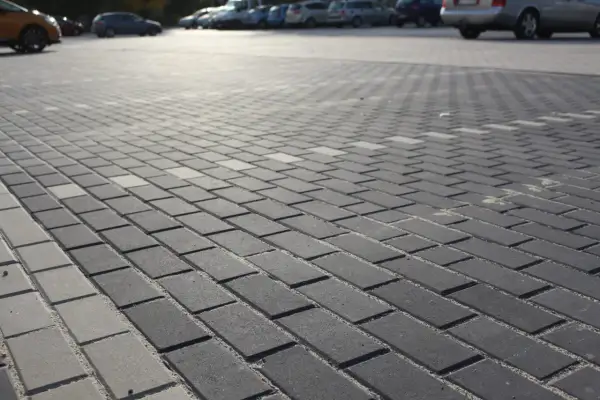 Szary parking wyłożony kostką holland. W tle widać zaparkowane samochody.