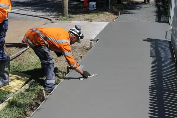Robotnik wygładza świeży beton B25. Cena za m3 jest kluczowa przy planowaniu budowy chodnika.